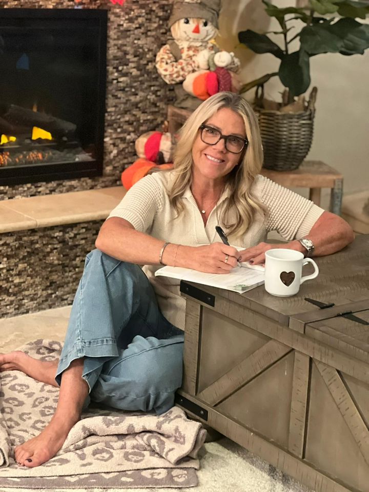 A reader sitting by her fireplace writing in The Divine Gratitude Journal.